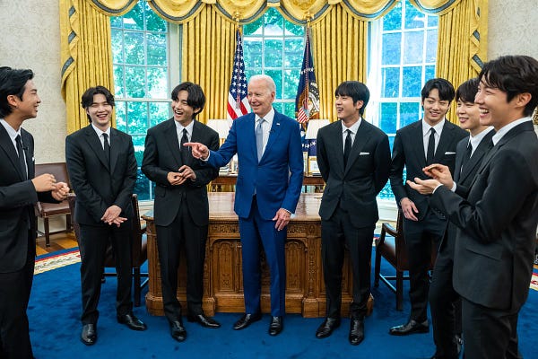 BTS stand in the Oval Office with President Biden. Everyone is smiling.