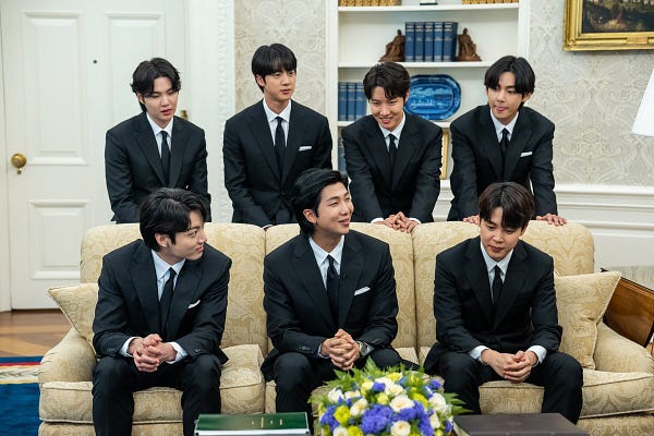 BTS sit in the Oval Office smiling.