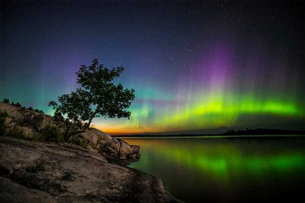 green, yellow, and purple northern lights swirl over a lake 