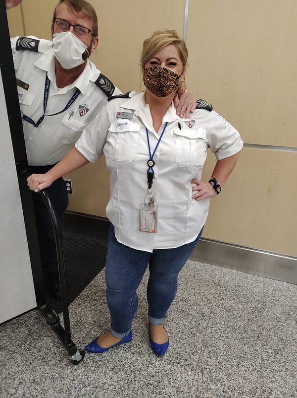 A male and female airport security screening officer standing inside an airport.