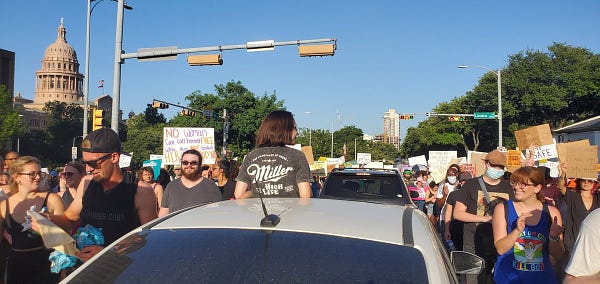 A driver gets out of her sun roof to cheer for the crowd. 