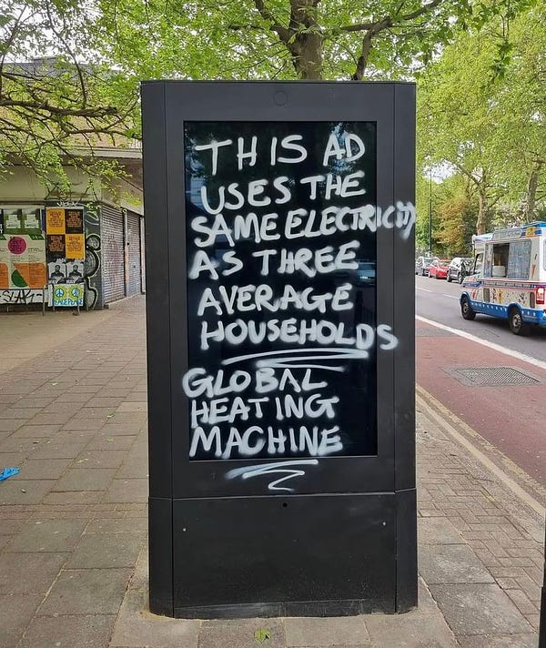 An electronic billboard which has been graffitied with the message - "This AD uses the same electricity as three average households. Global heating machine."