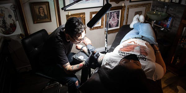Photo of a person laying down on a table receiving a tattoo on their left arm.