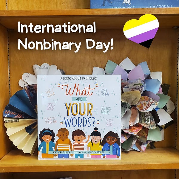 The book "What Are Your Words?" is displayed on a shelf with paper flowers behind it, and written on the image are the words "International Nonbinary Day!" next to a heart with the colors of the nonbinary flag.