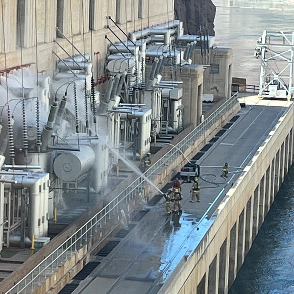 Firefighters seen with water hoses outside dam with water in distance