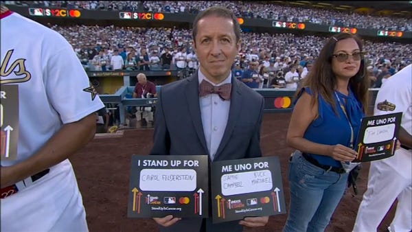 Ken Rosenthal holding up sign that reads "ME UNO POR JAMIE CAMPBELL BUCK MARTINEZ" for the "I Stand Up For Cancer" Campaign.