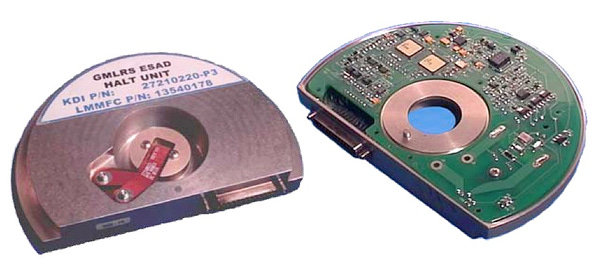 Top and bottom view of the "GMLRS ESAD halt unit". It's a semi-circle with a circuit board on one side. In the center is a red ribbon, probably attached to the ignitor. From "Guided MLRS Electronic Safety & Arming Devices (ESAD) & Electronic Safety & Arming Fuze (ESAF)" https://docplayer.net/102468905-Guided-mlrs-electronic-safety-arming-devices-esad-electronic-safety-arming-fuze-esaf.html