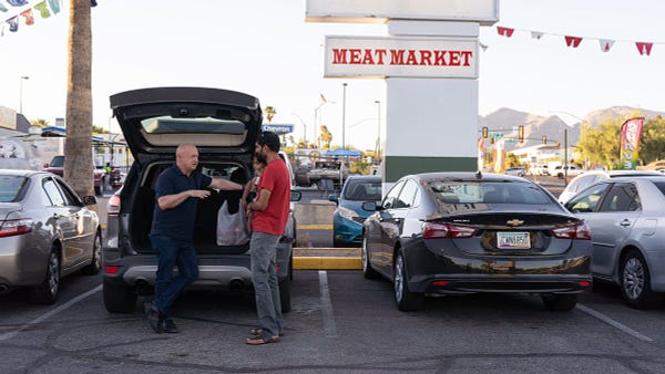 Mark Kelly leans on an American-made car while speaking with a parent outside a local Tucson carniceria.