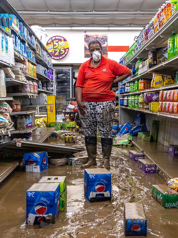 Gwen Christian, owner of Isom IGA in Isom, Kentucky, poses for a picture while standing in an aisle at her grocery store. A layer of mud and cases of soda are on the floor. 