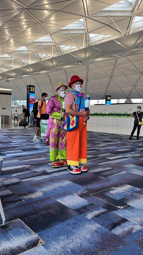Two clowns, one standing behind the other, preparing to juggle