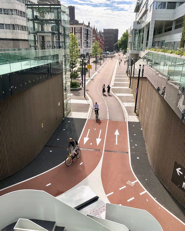Four cyclists ride on a wide, red bidirectional cycle path that enters directly into a parking facility underneath Utrecht Central Station.