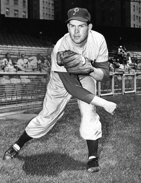 A black and white photo of Robin Roberts in a Phillies uniform. He looks like he just finished throwing a ball.