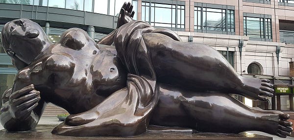 Massive figure lying on her right side on a large bronze slab. She is naked with a cloth over her loins. The figure, who is of exaggeratedly stylised thick proportion, has her face uplifted and clutches a ball in her right hand. Her left hand is open and pointing upwards and her right foot protrudes beyond the base.
