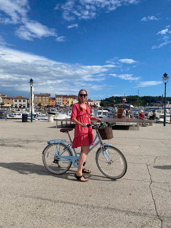 Me wearing a pink dress on a bicycle in a car-free zone - boats and houses in the background.