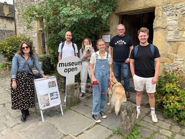 6 people and 2 dogs are standing smiling outside a beautiful old Tudor building, with a sign saying ‘museum open’