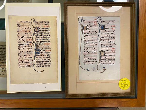 Two pages from a 13th century manuscript. Both have musical notation and decorated initials. The vellum on unframed leaf on the left has yellowed with age, while the vellum on the framed leaf on the right is quite white, much closer to how the manuscript would have looked when it was initially produced