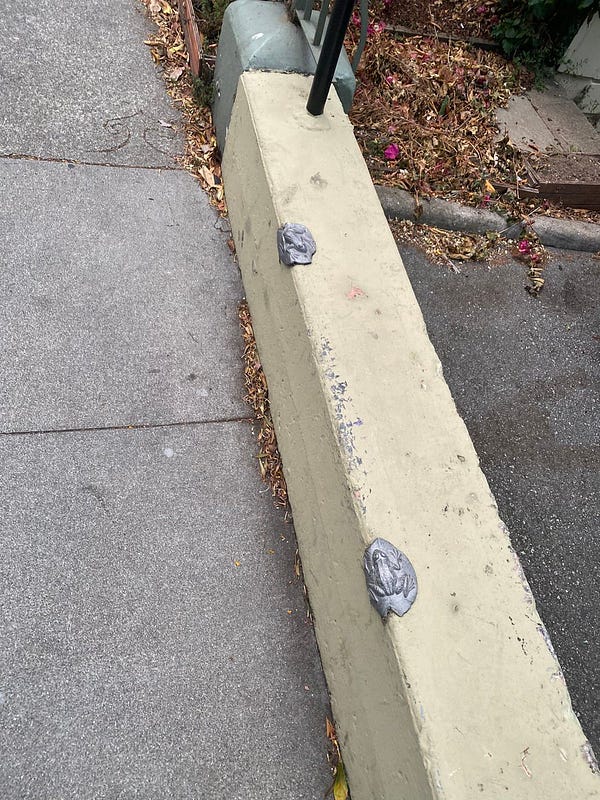 Cream colored curb along sidewalk with metal badges in the shape of frogs along the edge to prevent skateboarding