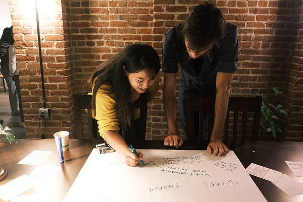 Two people are writing on a piece of poster paper.