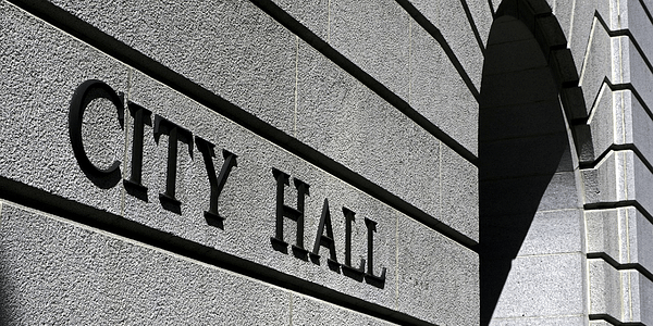 Black and white image of a close up of a building with City Hall engraved on the side next to an arch.