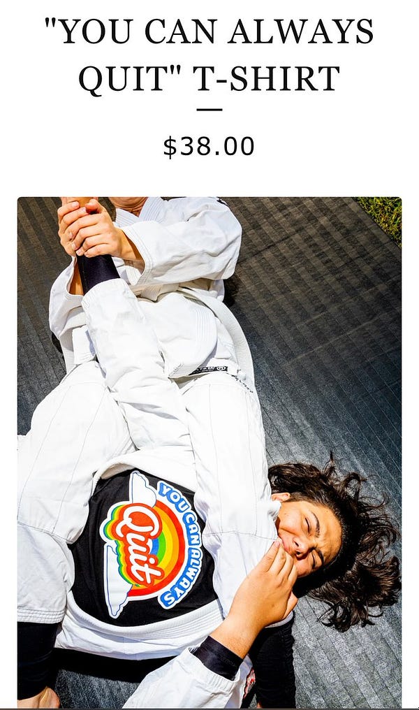 Two judoka are wrestling in bright white kimonos, the one whose arm is about to be snapped in half at the elbow is wearing a shirt with a rainbow and real puffy clouds that says, “you can always QUIT”.