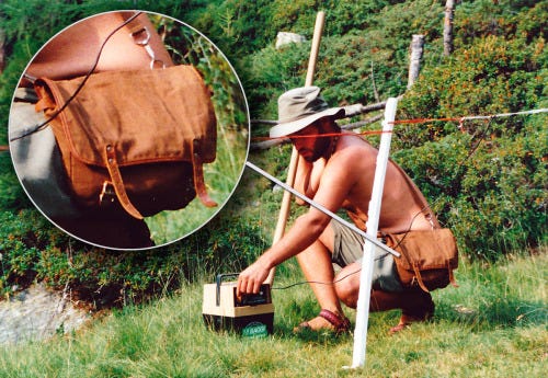 A younger @Documentally in shorts, sandals & sporting a Tilley hat sets up a self timed photo on a film camera while working on an isolated mountain in the Swiss alps. 

Having set up an electric fence to ensure a herd of young cows making their way up the mountain do not descend, he is crouching to turn it on. 

Hanging round his neck is a brown canvas satchel with leather straps. Inside the bag is a knife, some fresh flatbread and a chunk of cheese. There is something else but you will have to read his weekly email to find out what it is. It can be found on http://Documentally.net
