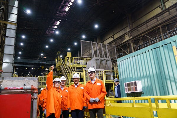 Prime Minister Justin Trudeau, Minister Francois-Philippe Champagne, Lakshmi Mittal, and Ron Bedard are standing inside an industrial facility. Minister Champagne is pointing into the distance.
