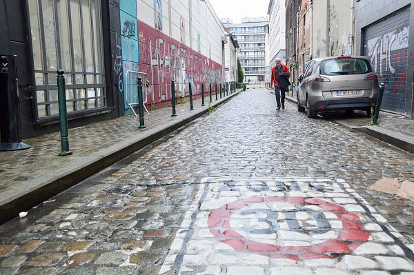 A red-and-white 30 km/h speed limit road marking painted on a cobbled street in Brussels. A man walks in the background.