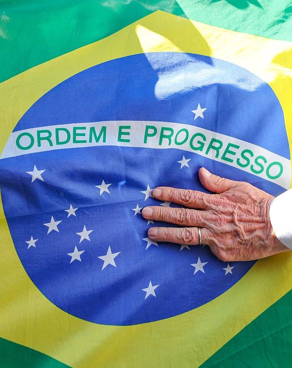 Mão de Lula repousa em bandeira do Brasil.