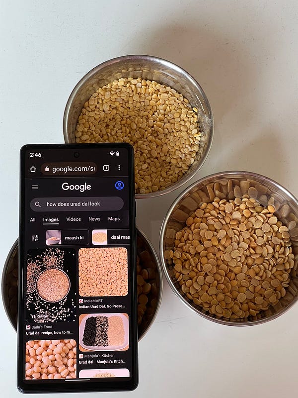 A phone with the Google Chrome app open, with ‘how does urad dal look’ written in the Search box, placed on top of bowls filled with different dals.