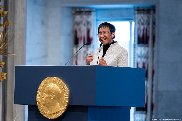 Maria Ressa speaking on 10 December 2021. She is delivering her Nobel Prize lecture wearing a white blazer and glasses. 