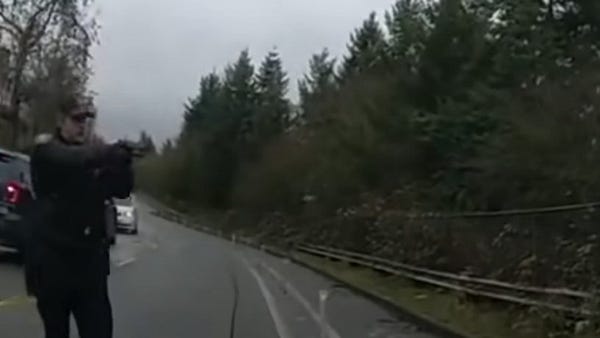 Still from a police body cam showing officer Timothy Jones wearing a rain jacket and a baseball cap standing on a city street with his gun drawn. 