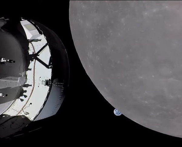 The Orion spacecraft captures an image of Earth setting behind the Moon. The metallic grey and white structure of the spacecraft dominates the left side of the image. To the far right, the dusty grey surface of the Moon looms large beside the small blue and white Earth in the far distance. The background of the image is the dark blackness of space. No stars are visible as the high contrast of the Moon and Orion spacecraft wash out the distant stars. Credit: NASA