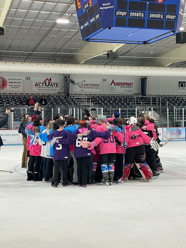 Team Trans huddling up at center ice in a group hug. 