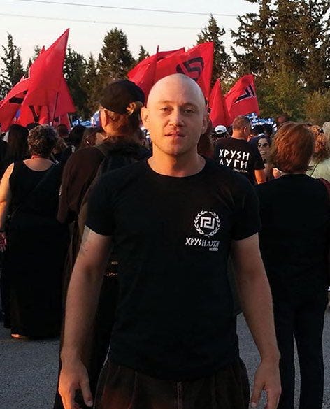 photo shows a man with a shaved head in black in front of red flags