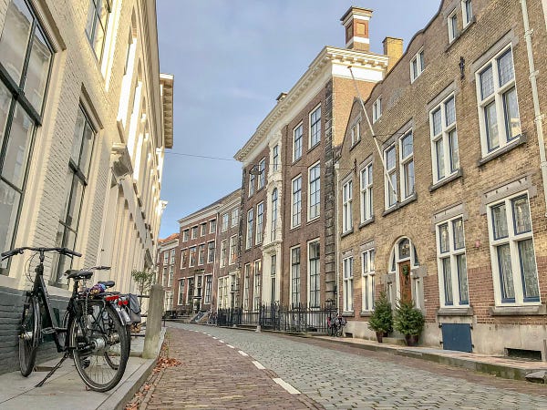 A narrow, cobblestone, car-free street in the Dutch city of Middelburg is lined with three-storey buildings, wooden benches, planter boxes, and parked bikes.
