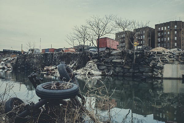 Bronx River with tires and debris in river and trucks on cliff in background.