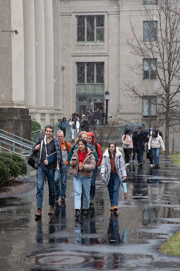 Students walk on a wet walkway while light snow falls