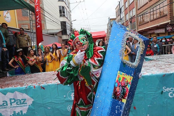 Pepino, personagem popular boliviano, em pé, segurando a tampa do Caixão. Ao fundo é possível ver uma plateia.