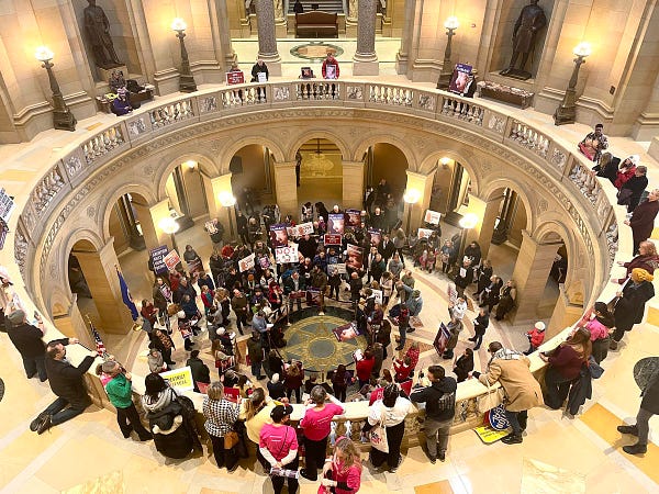 a circle of people carrying signs with pro-life messaging gathers in the Minnesota Senate rotunda, surrounded by an outer ring of pro-choice advocates