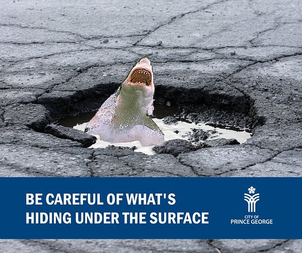 A shark jumps menacingly out of a puddle in a pothole. Graphic text reads "be careful of what's hiding under the surface"