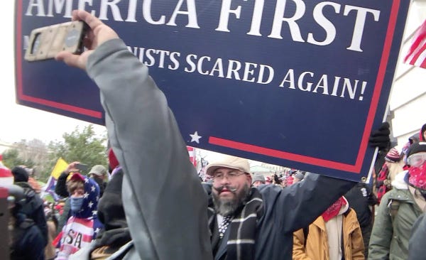 Fredy Burgos in a restricted area at the US Capitol on January 6th 2021. He is holding a large America First "Make Communists Scared Again" sign, surrounded by other rioters.

