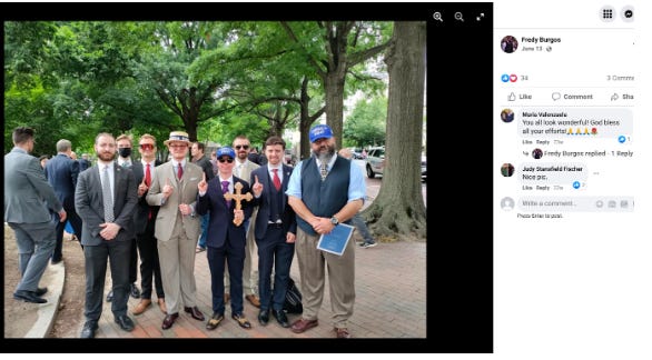 Group of young white men dressed in suits one middle age one in a vest, tie and short sleeve blue shirt at an anti choice rally.

The two to the furthest left are Joseph Brody aka #SuitGuy and Paul Lovley aka #BrownSweaterBrat (wearing a mask) 

One, much shorter than the rest is holding a wood cross and wearing a purple tie and blue baseball cap with the words America First on it. He is often seen with Burgos at events carrying a blue America First logo flag. 