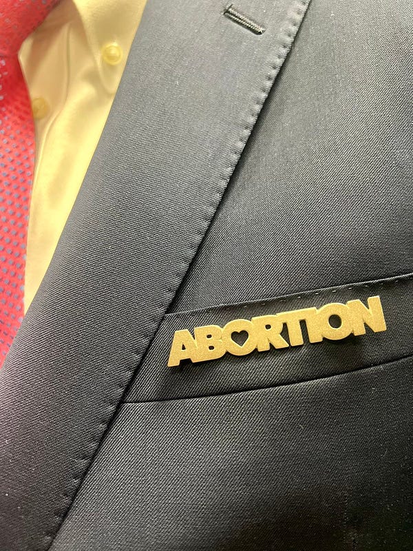 A close up of the gold abortion pin on Ed’s pocket