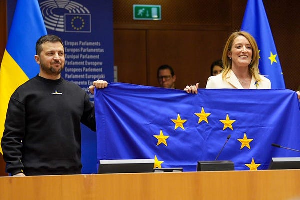 The President of the European Parliament Roberta Metsola and the President of Ukraine Volodymyr Zelenskyy holding the flag of the European Union.