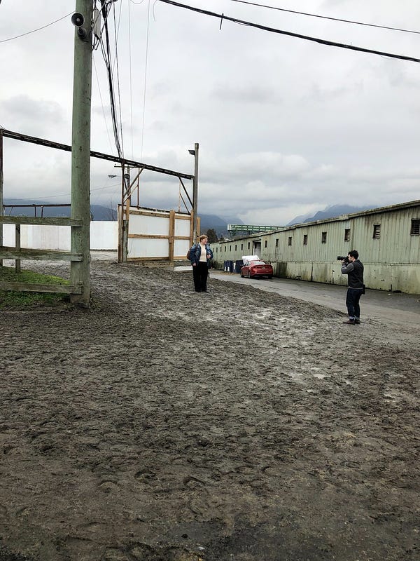 Woman and photographer standing in front of an open gate where horses exit a racetrack. 