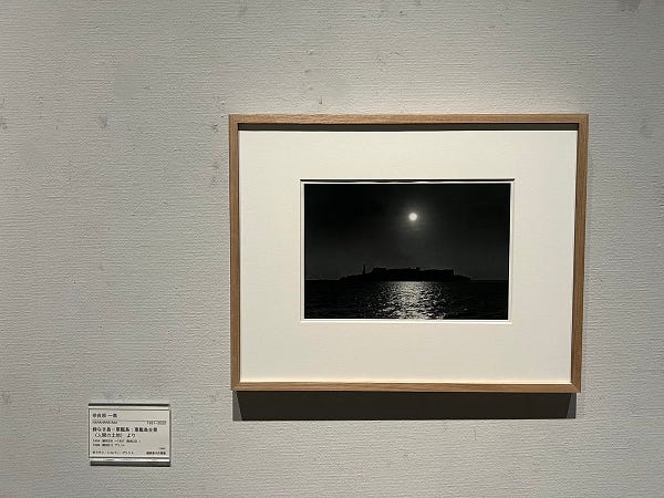 Gunkanjima at night with the moon in the sky. Black and white photo by Narahara Ikkō.