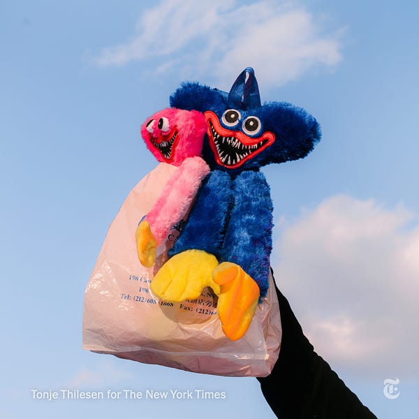 A hand holds up two plushie dolls of Huggy Wuggy, a video game character that has become popular with children. Photo by Tonje Thilesen for The New York Times.