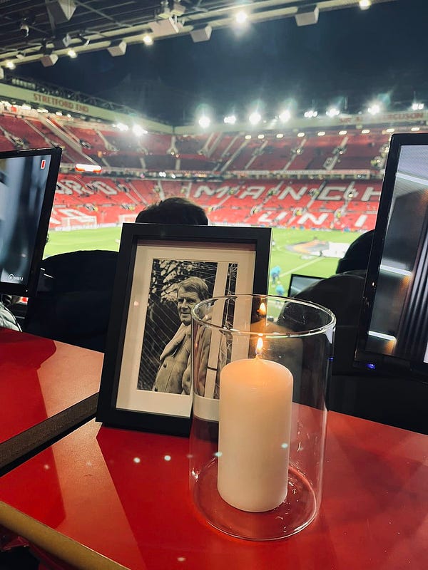An image of John Motson laid in commentary position at Old Trafford, with a candle lit next his photo.