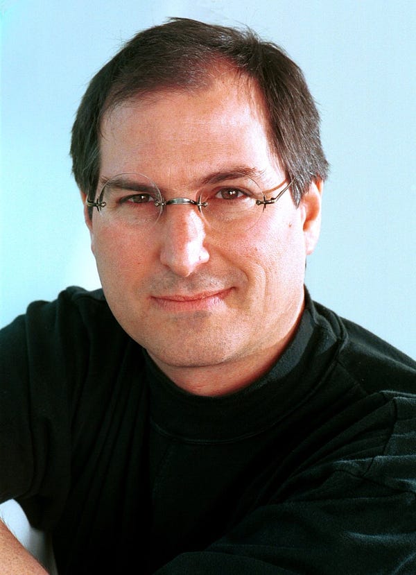 A portrait of Steve smiling in glasses and a black turtleneck from 1996.