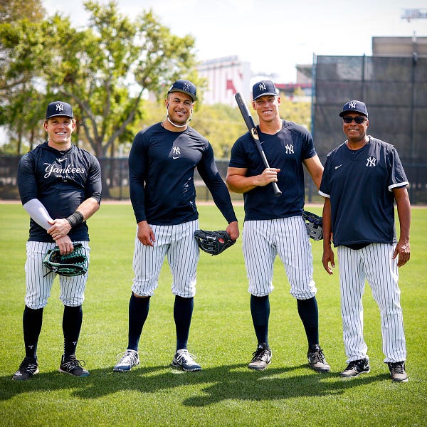 Harrison Bader, Giancarlo Stanton, Aaron Judge, and Bernie Williams pose for a photo in the outfield during a Spring Training workout. 